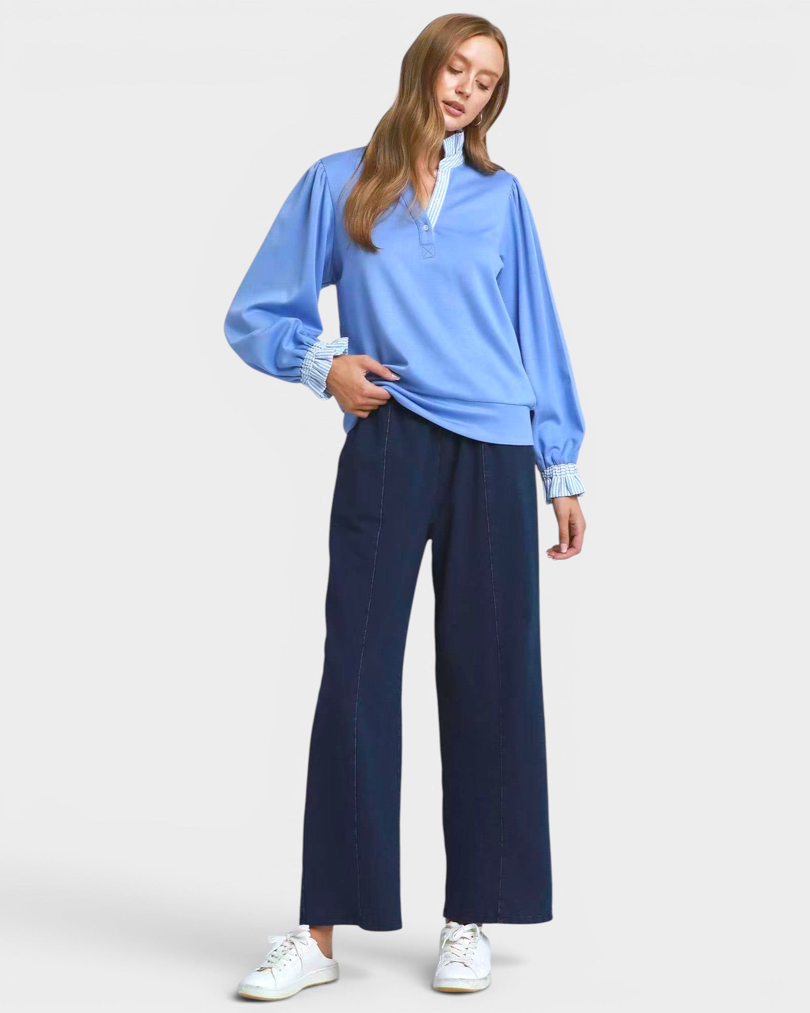 Woman wearing a blue long-sleeve top and navy pants on a white background