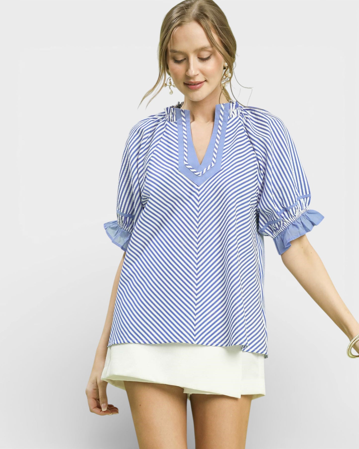 Woman wearing a blue and white striped blouse with rolled-up sleeves on a plain background