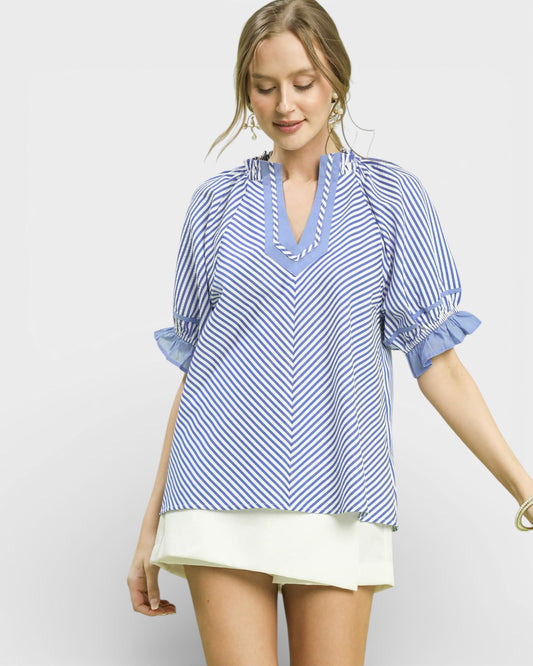 Woman wearing a blue and white striped blouse with rolled-up sleeves on a plain background