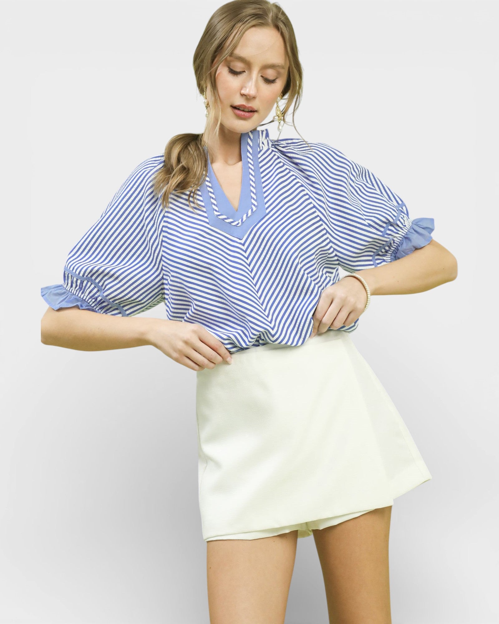 Woman wearing a blue and white striped blouse and cream skirt on a light gray background