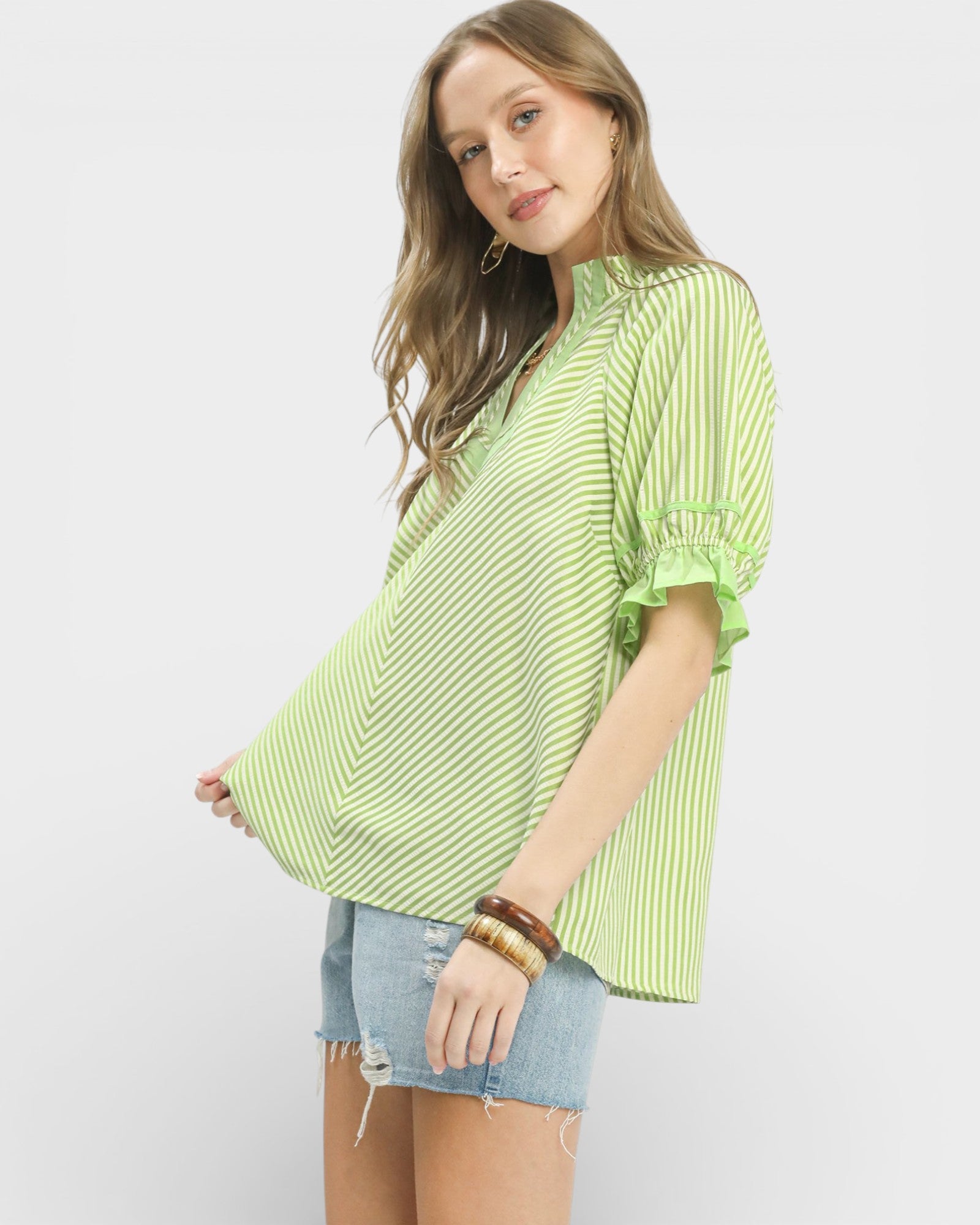 Woman wearing a green striped shirt and denim shorts on a white background
