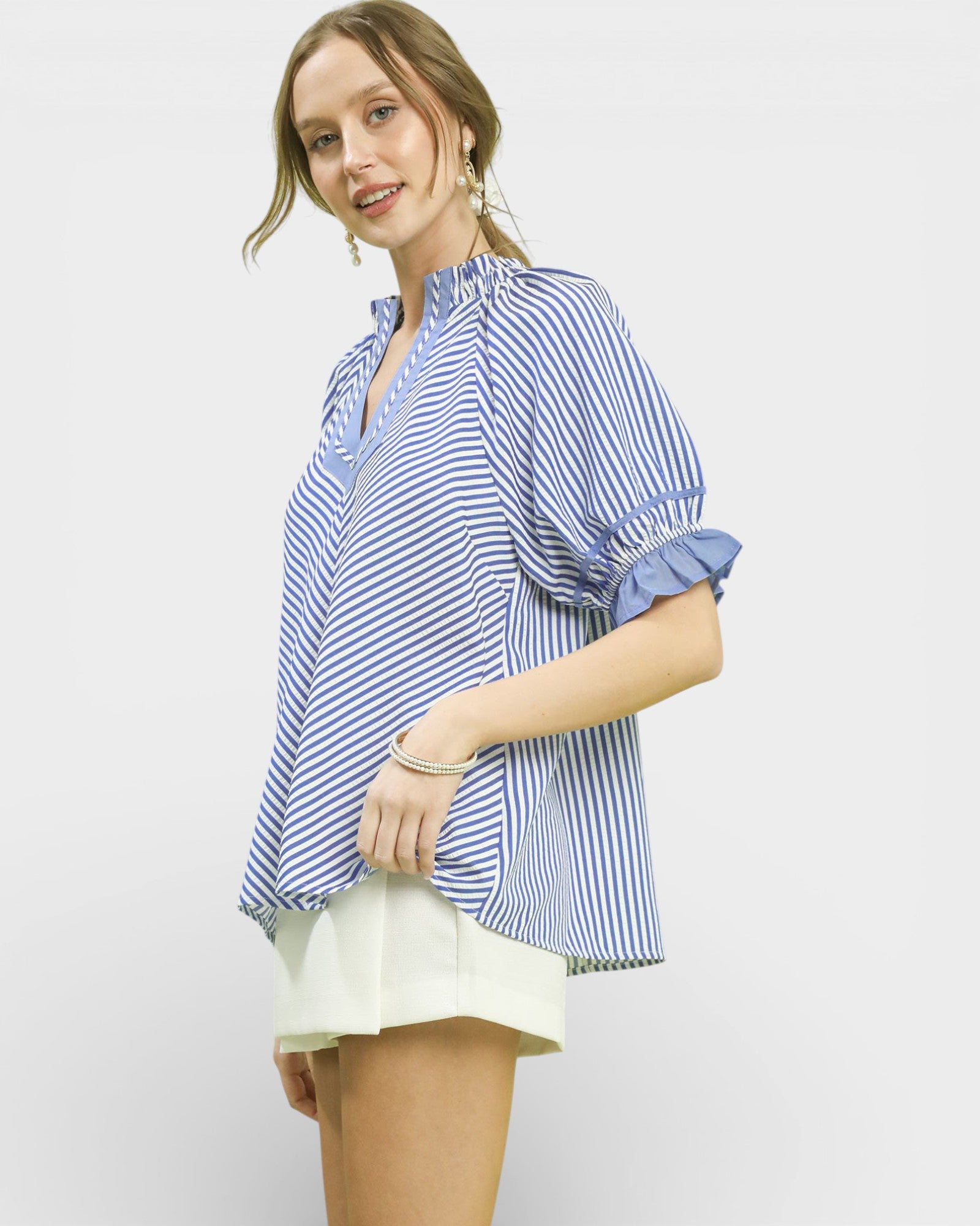 Woman wearing a blue and white striped shirt with rolled-up sleeves on a light gray background