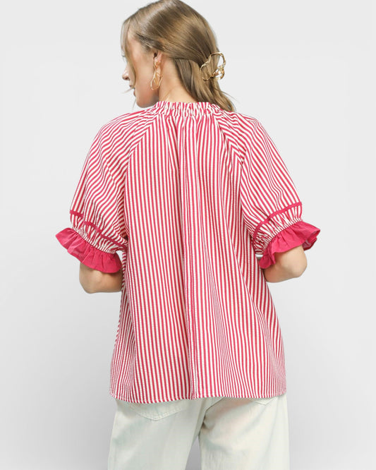 Woman wearing a red and white striped blouse with ruffled sleeves on a light gray background
