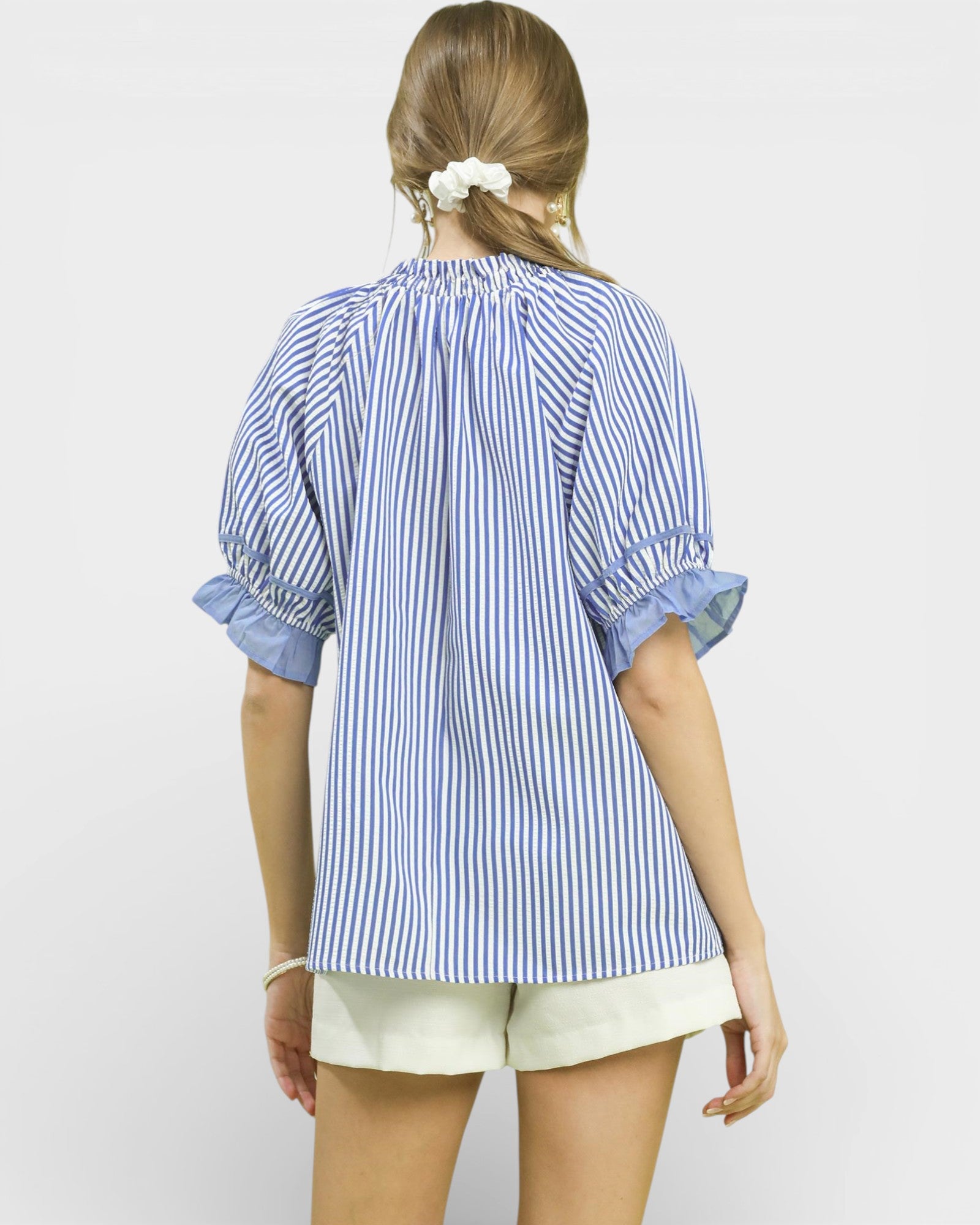 Woman wearing a blue and white striped shirt with rolled-up sleeves on a plain background