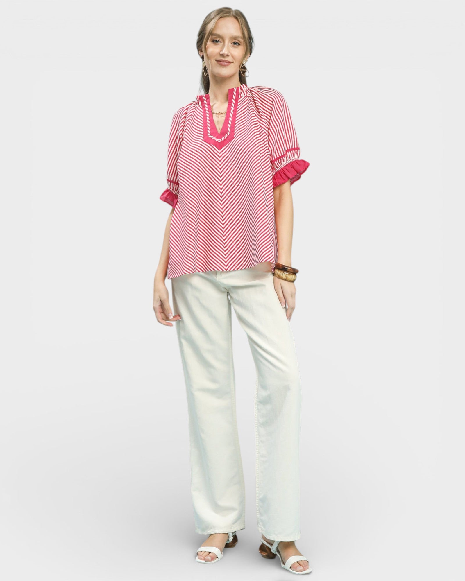Woman wearing a red and white patterned top with white pants on a light gray background