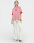 Woman wearing a red and white patterned top with white pants on a light gray background