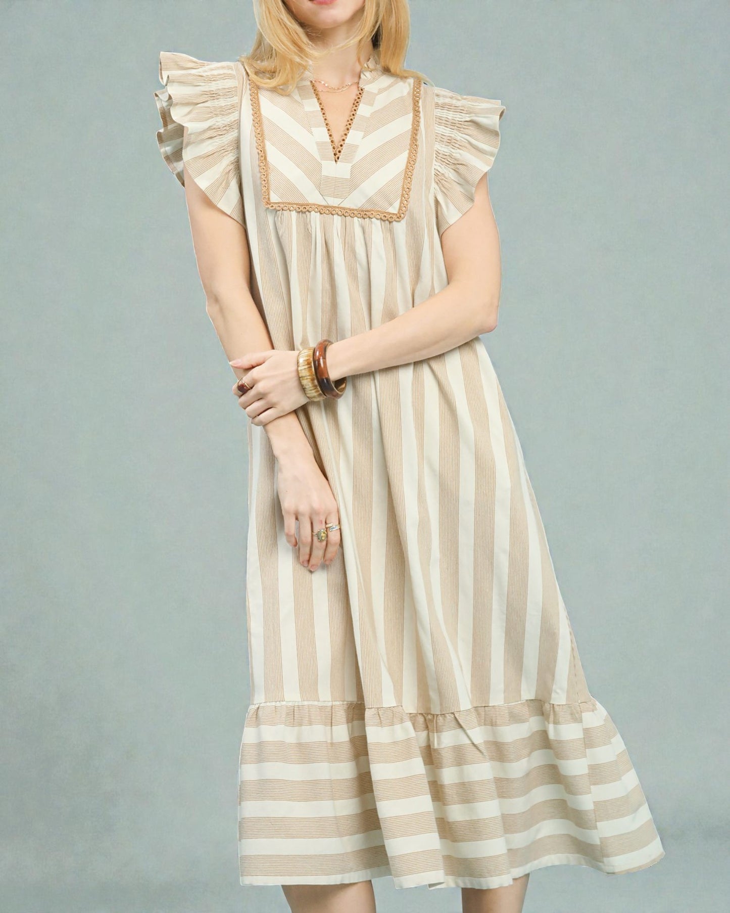 Woman wearing a beige and white striped dress on a gray background