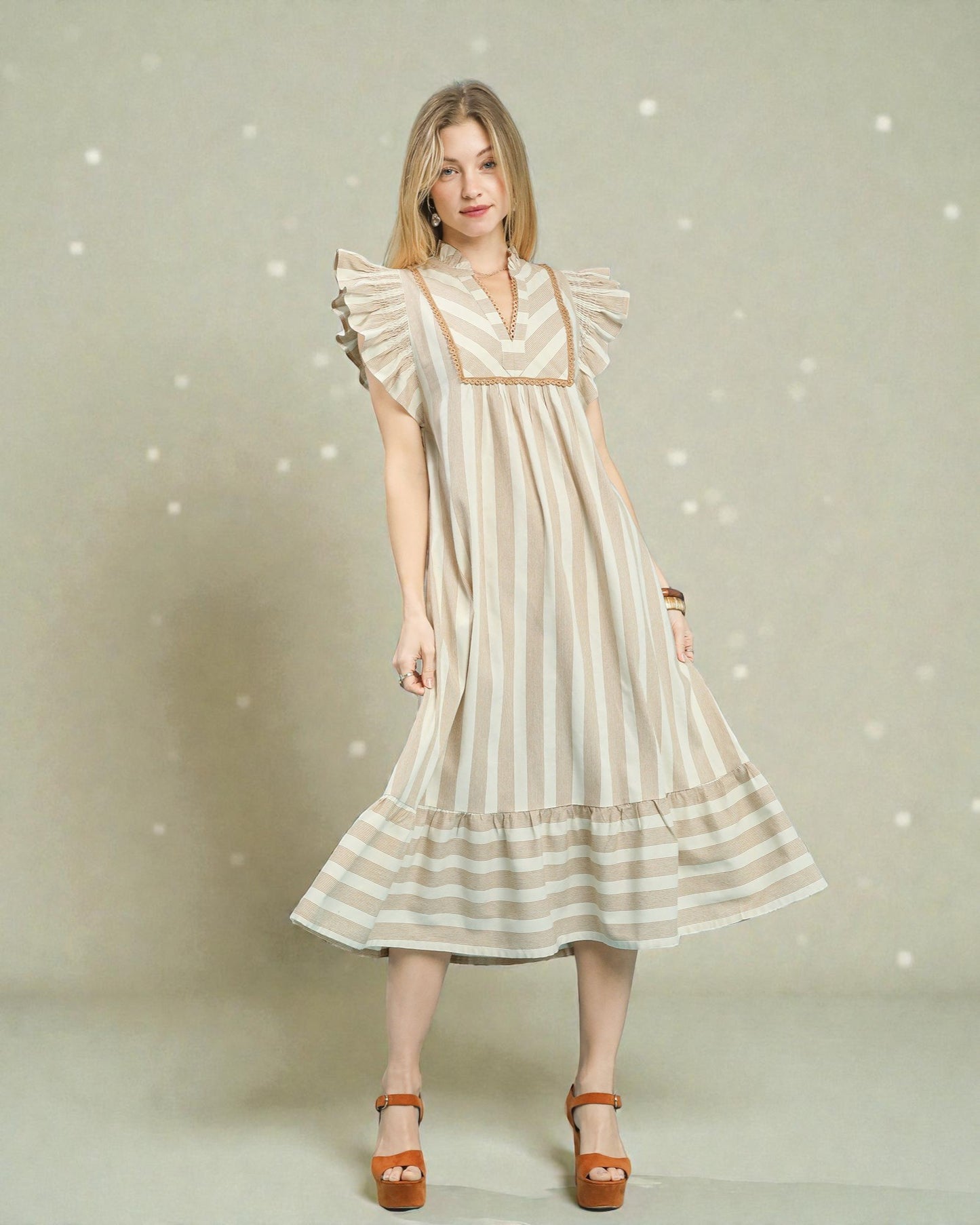 Woman wearing a beige and white striped dress with ruffled sleeves against a light background