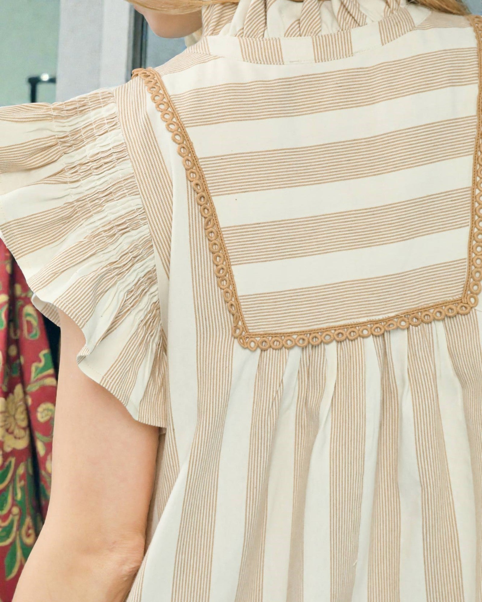 Close-up of a beige and white striped dress with ruffled sleeves.