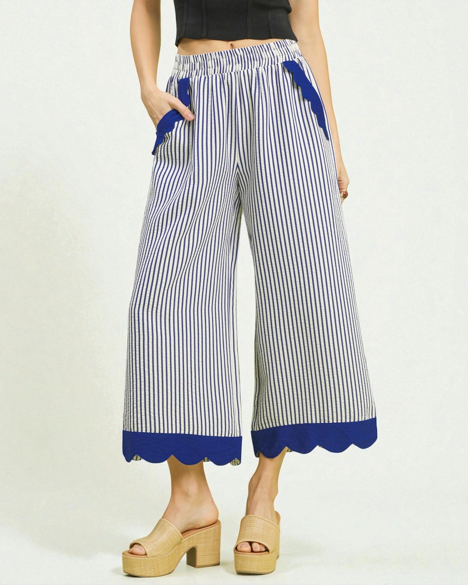 Woman wearing blue and white striped pants with scalloped hem on a plain background