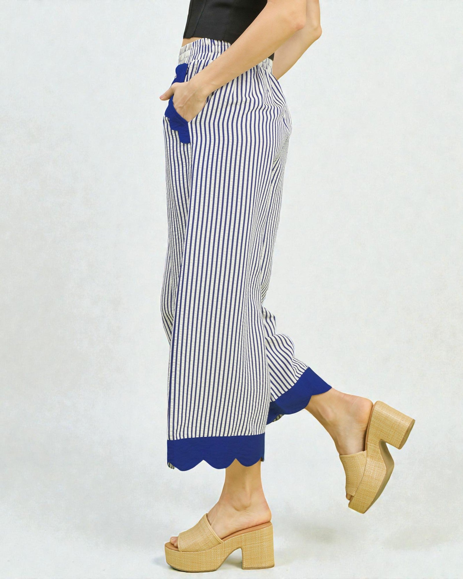 Person wearing blue and white striped pants with scalloped hem on a white background