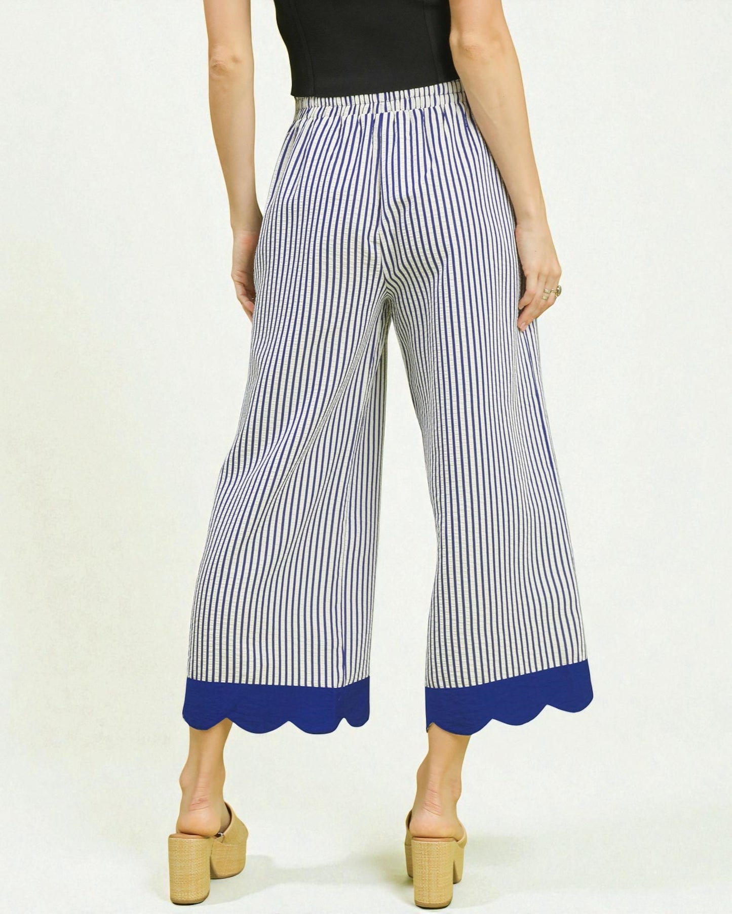 Woman wearing blue and white striped pants with a scalloped hem on a white background