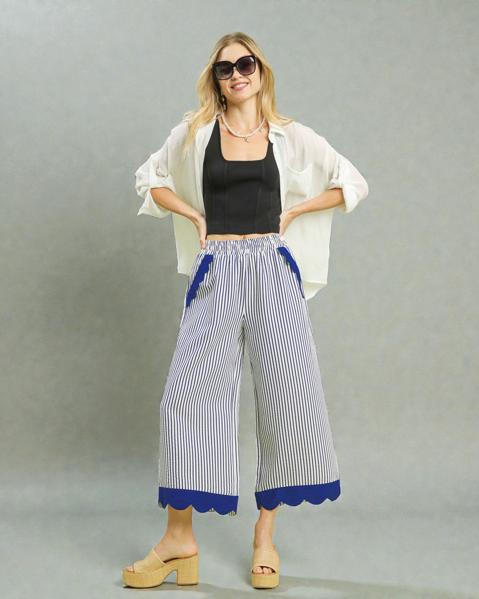 Woman wearing a white jacket, black top, and blue and white striped pants on a gray background