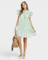Woman wearing a light green dress holding a beige handbag on a white background