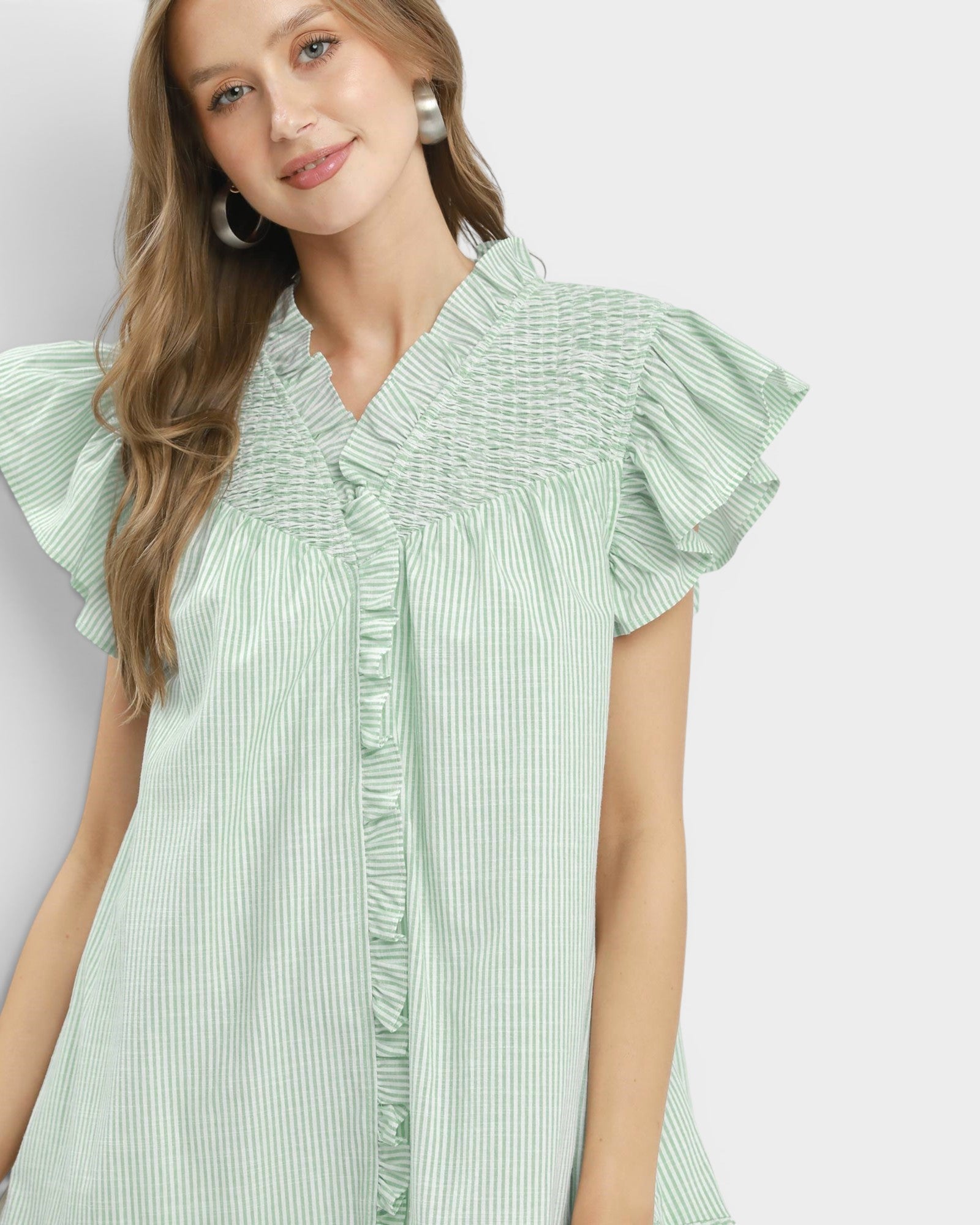 Woman wearing a green striped dress with ruffled sleeves on a white background