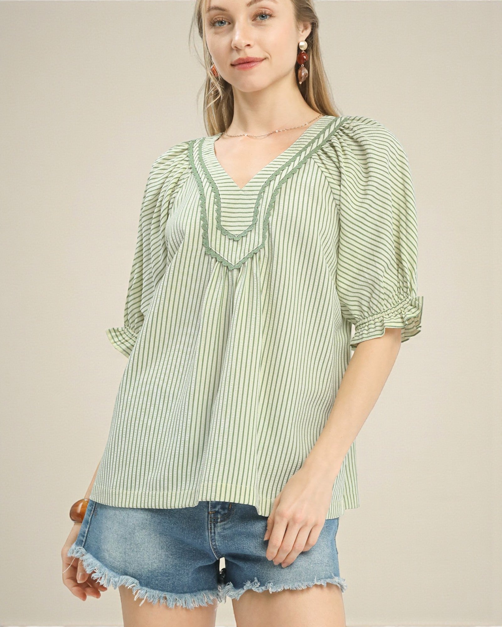 Woman wearing a green and white striped blouse with denim shorts on a beige background