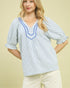 Woman wearing a blue and white striped blouse with ruffled neckline against a beige background