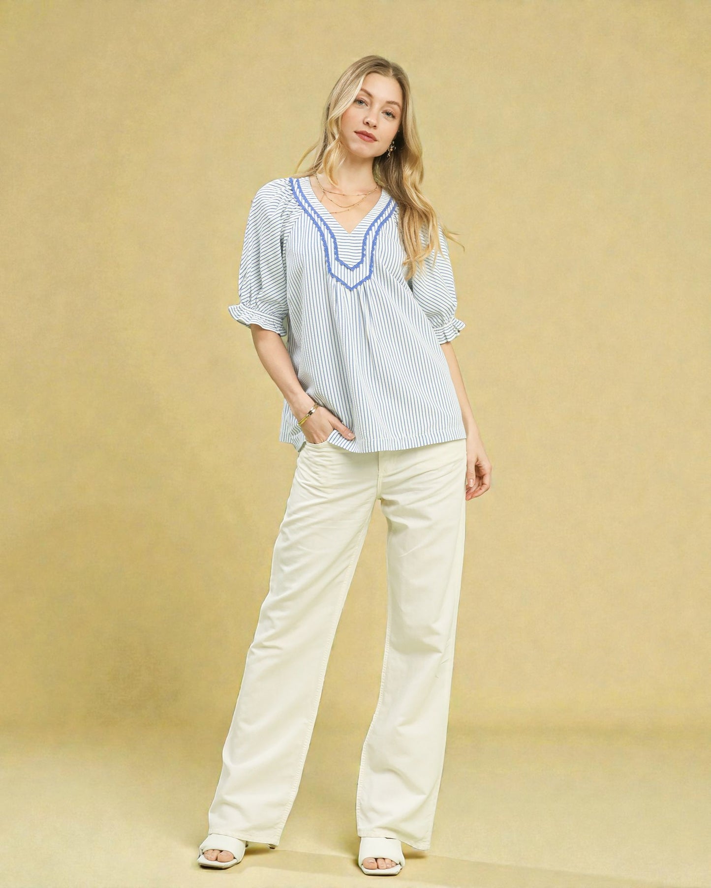 Woman wearing a striped blouse and white pants against a beige background