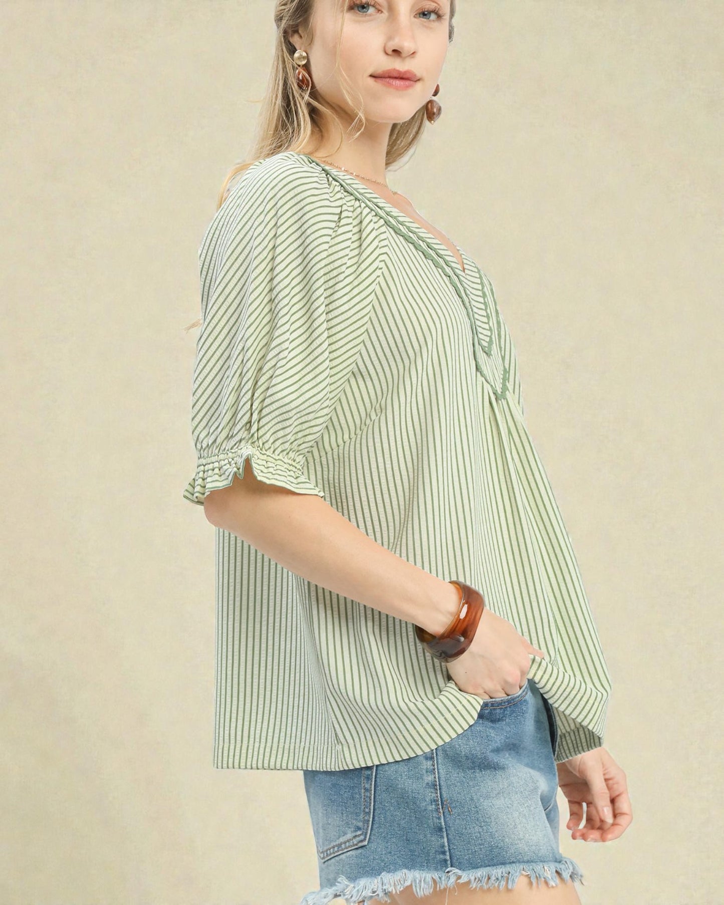 Woman wearing a green and white striped blouse with denim shorts on a beige background
