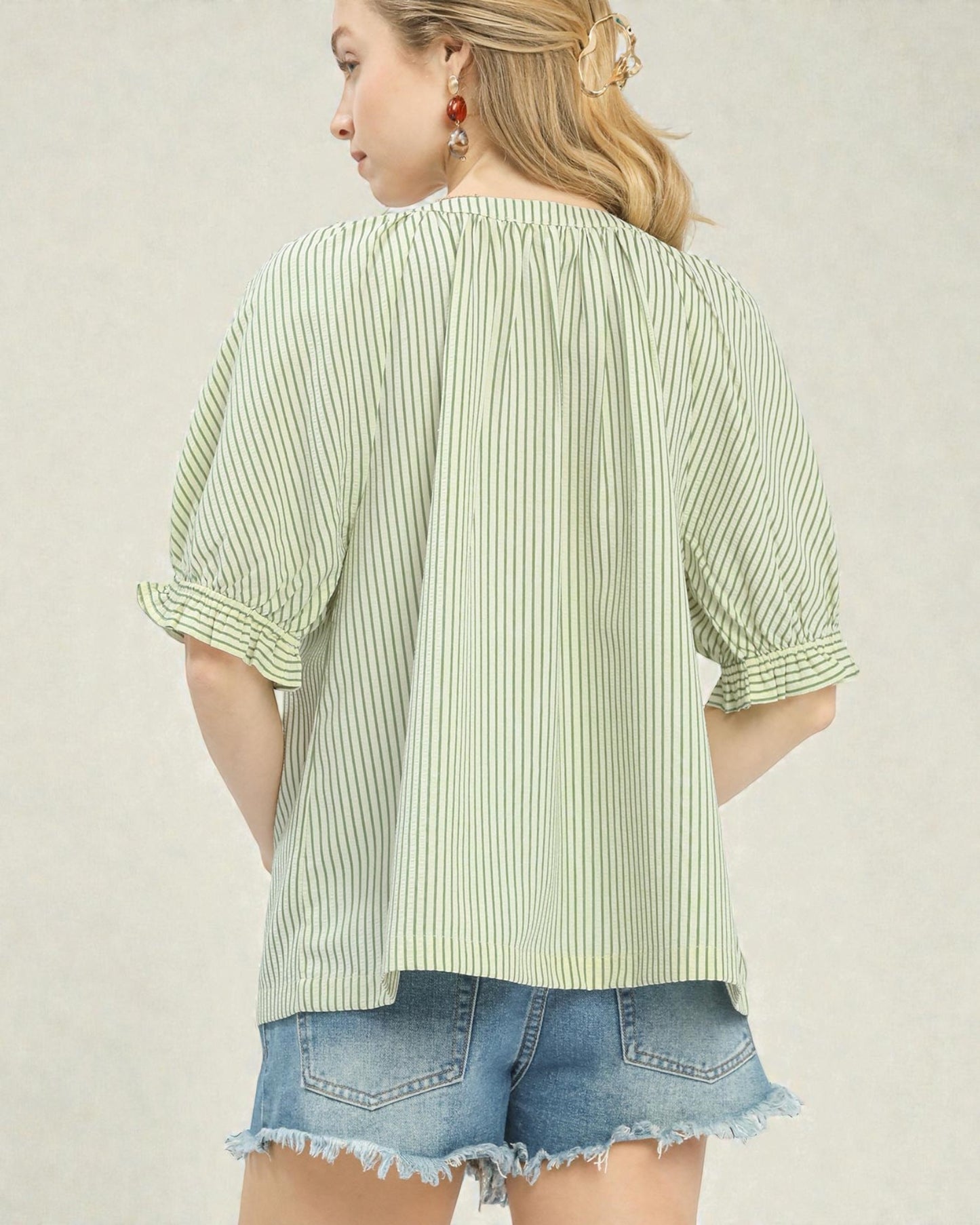 Woman wearing a green and white striped shirt with denim shorts on a plain background