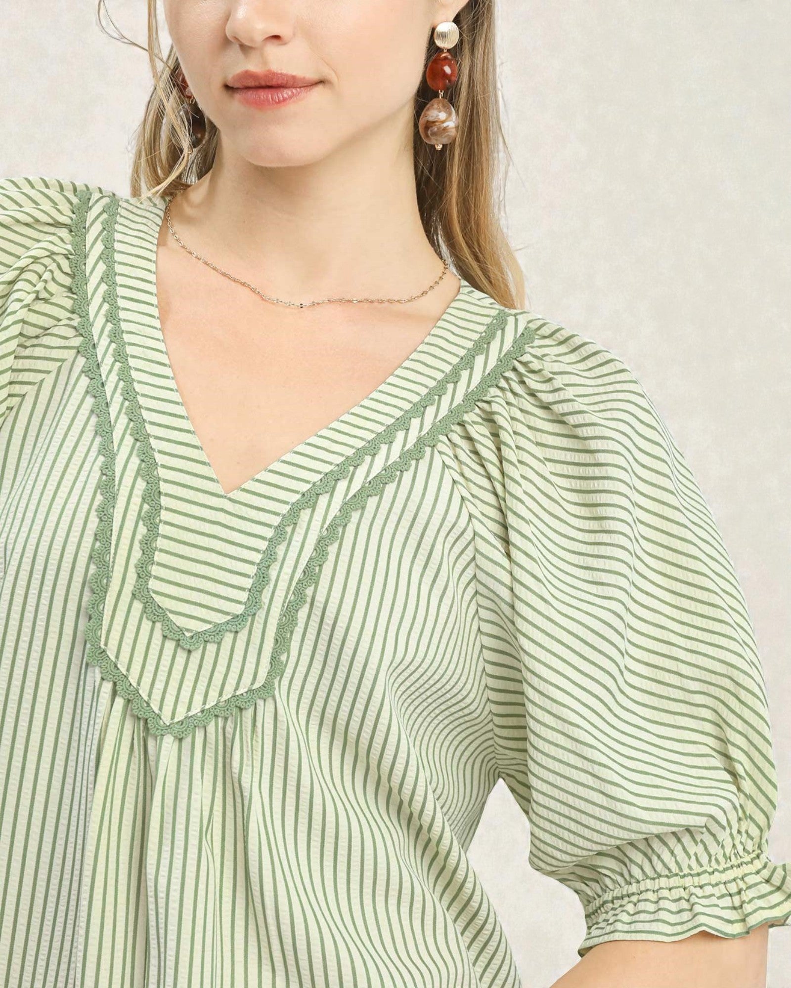 Green and white striped blouse with ruffled neckline on a plain background