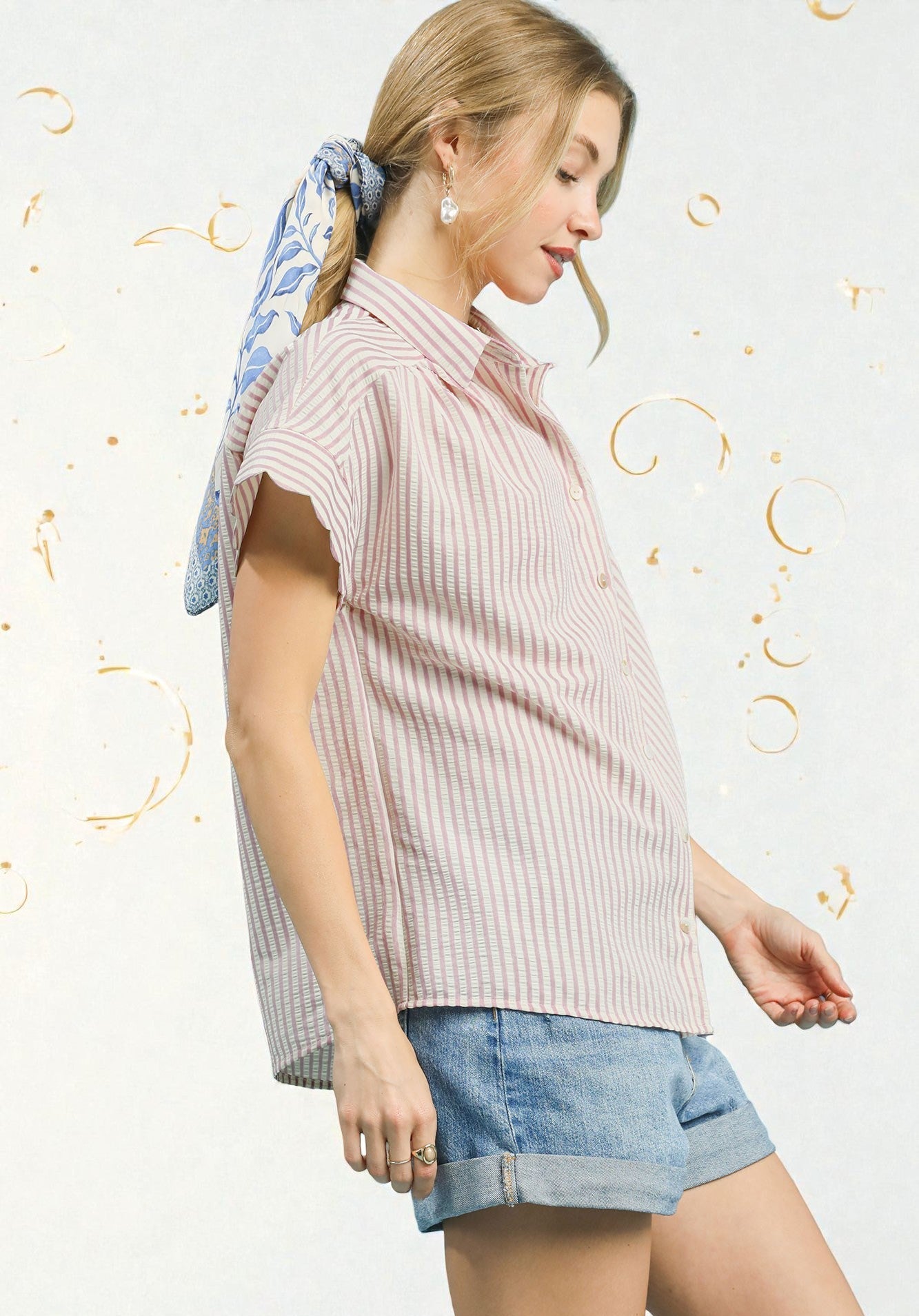 Woman wearing a pink striped blouse and denim shorts with a decorative headscarf on a light background