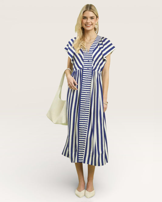 Woman wearing a blue and white striped dress holding a beige handbag on a light background