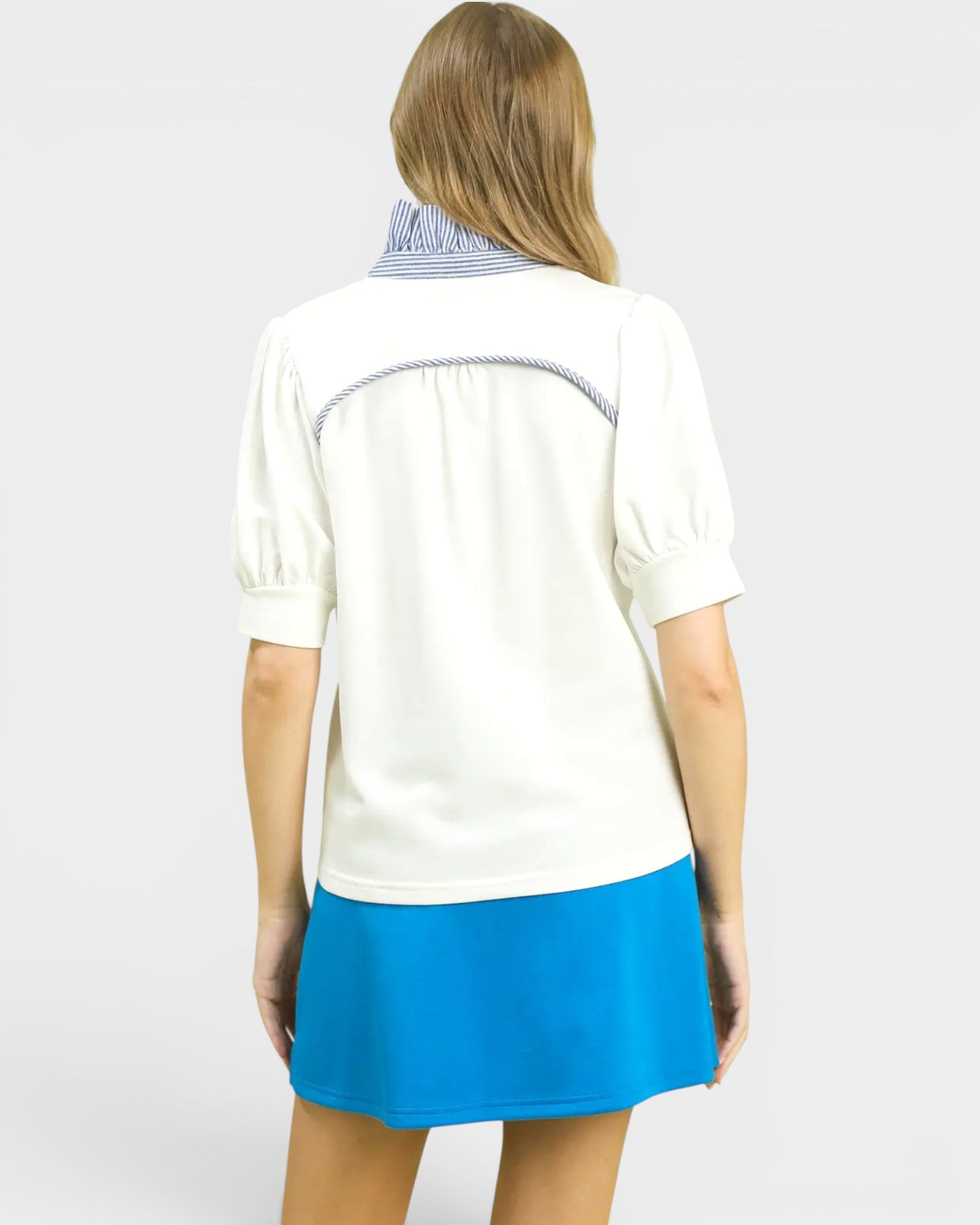 Woman wearing a white blouse with a blue skirt on a plain background
