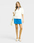 Woman wearing a white blouse and blue skirt with a beige bag on a light gray background