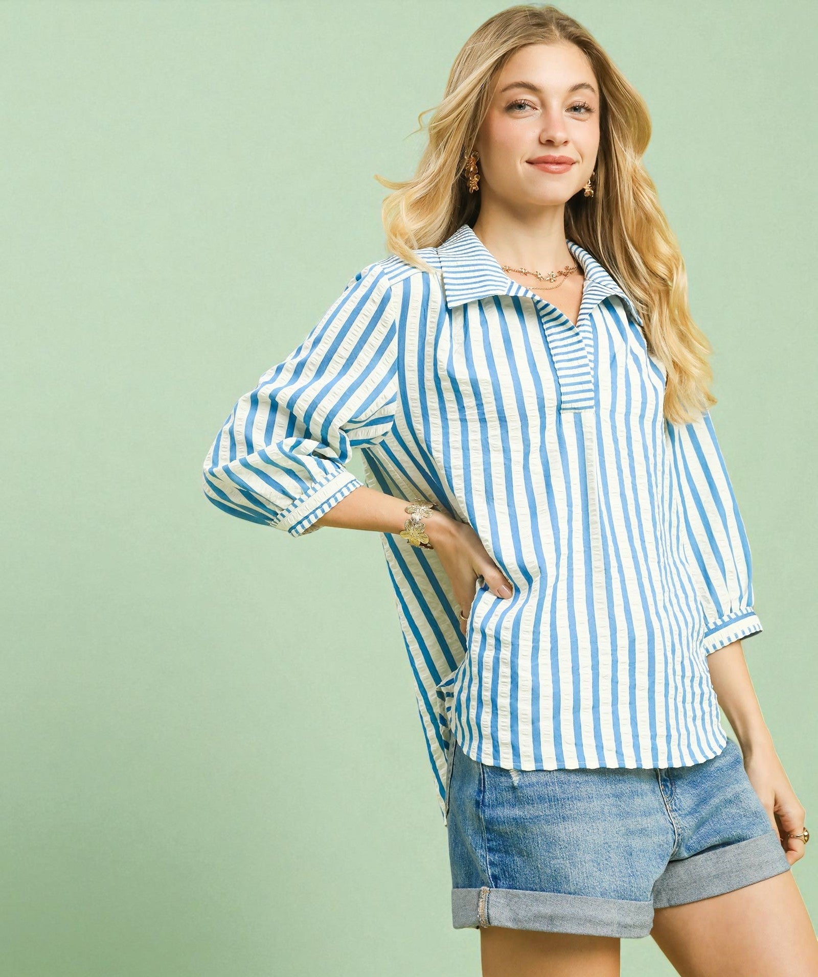 Woman wearing a blue and white striped shirt with denim shorts on a light green background