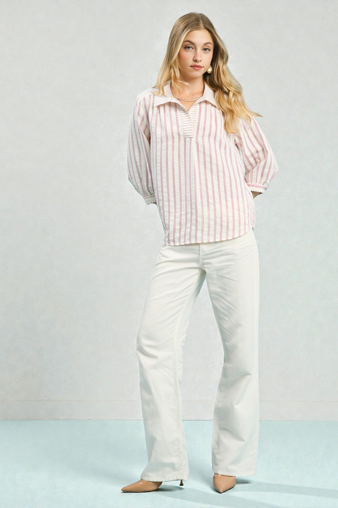 Woman wearing a striped shirt and white pants on a light background