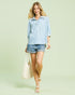 Woman wearing a blue and white striped shirt and denim shorts against a light green background