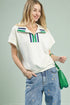 Woman wearing a white polo shirt with colorful accents and blue jeans, holding a green bag.