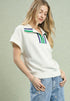 Woman wearing a white polo shirt with colorful stripes and blue jeans on a light green background