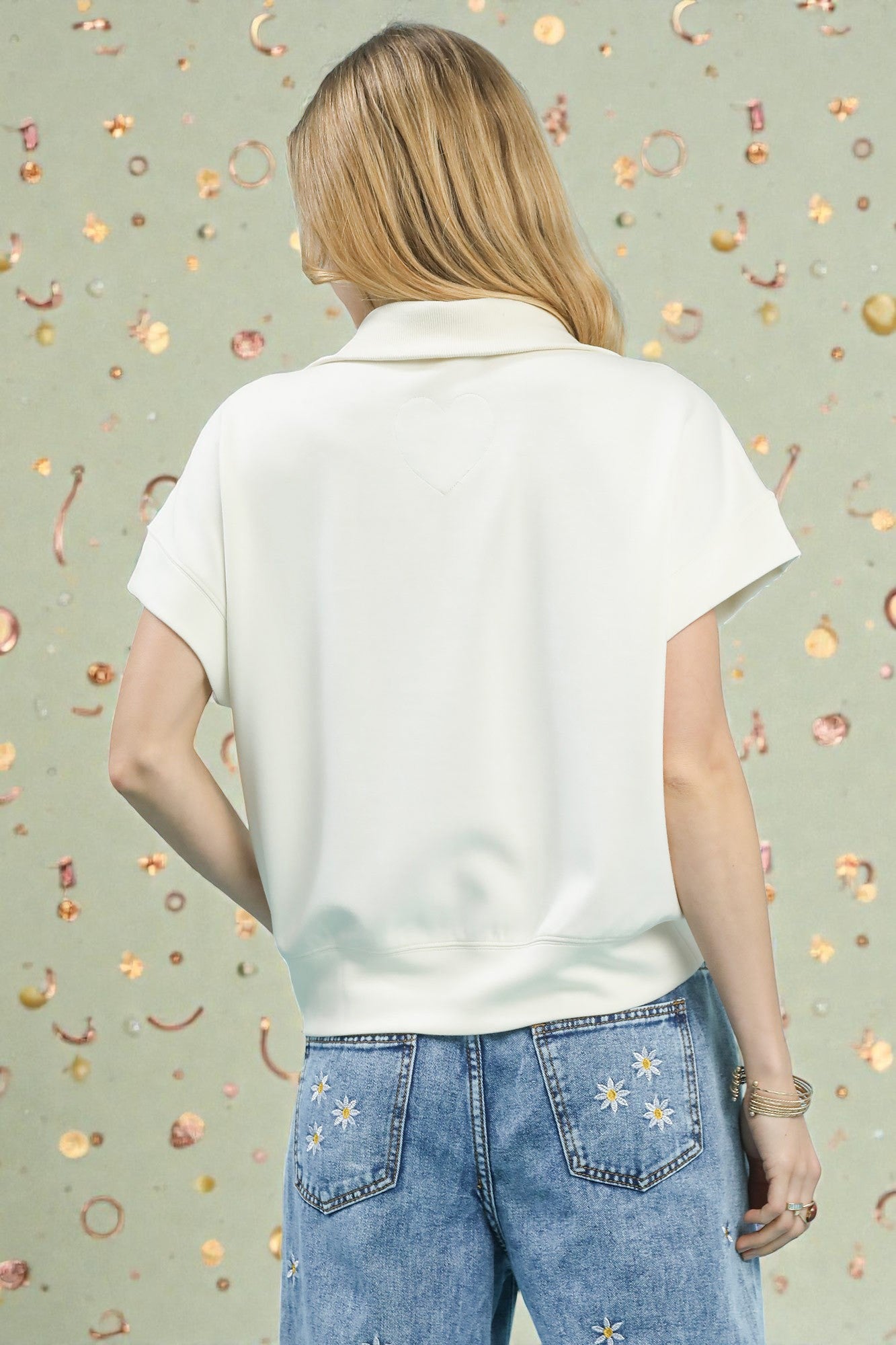 Person wearing a white polo shirt and blue jeans with floral designs on a patterned background