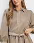 A woman wearing a taupe-brown long-sleeve dress with a striped collar, button placket, cuffs, and waist tie, shown in a close-up studio shot.