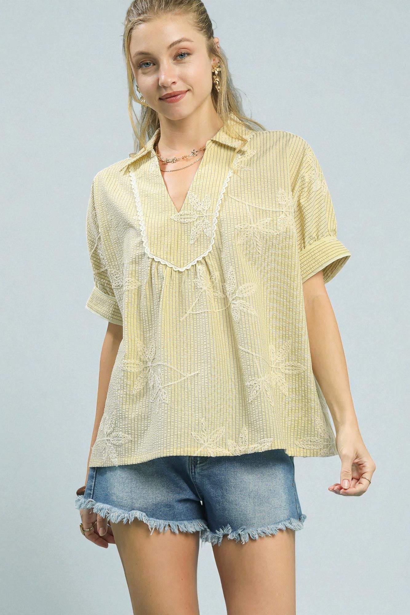 Woman wearing a yellow striped shirt and denim shorts on a light gray background