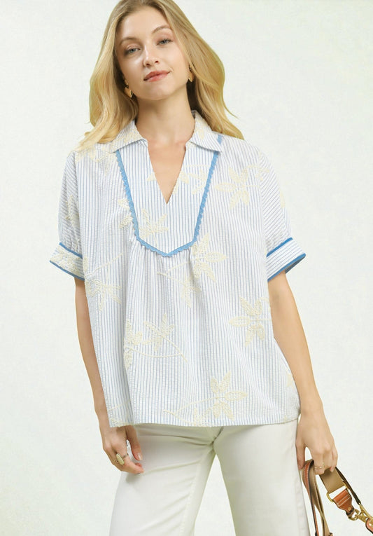 Woman wearing a white blouse with blue accents and white pants on a white background