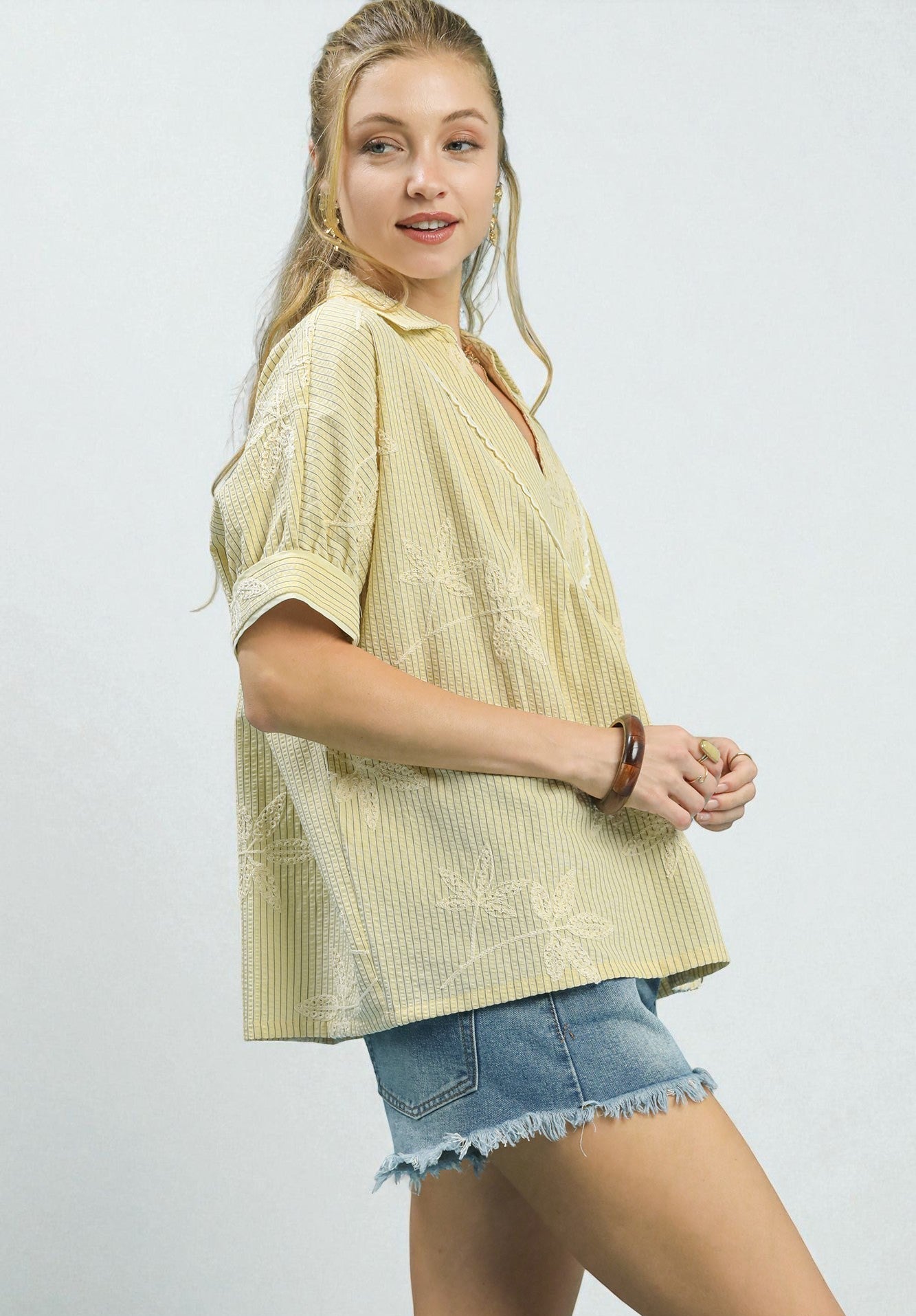 Woman wearing a light yellow patterned shirt and denim shorts on a white background
