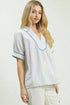 Woman wearing a light blue and white striped blouse with floral patterns on a plain background