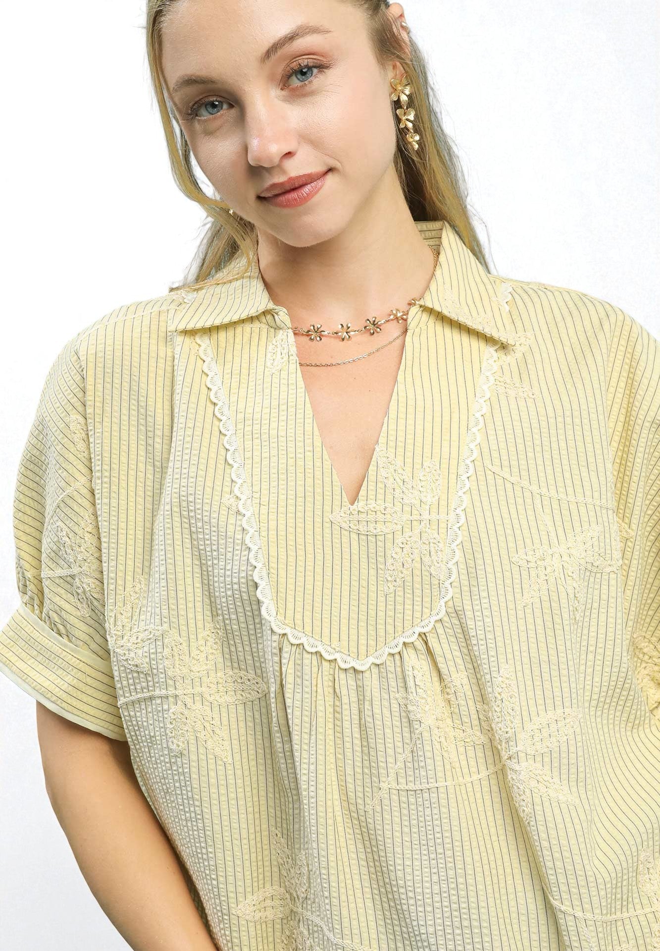 Woman wearing a light yellow blouse with a white collar against a white background