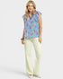 Woman wearing a blue floral blouse and white pants on a white background