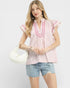 Woman wearing a pink and white striped blouse with ruffled sleeves and denim shorts on a light gray background.