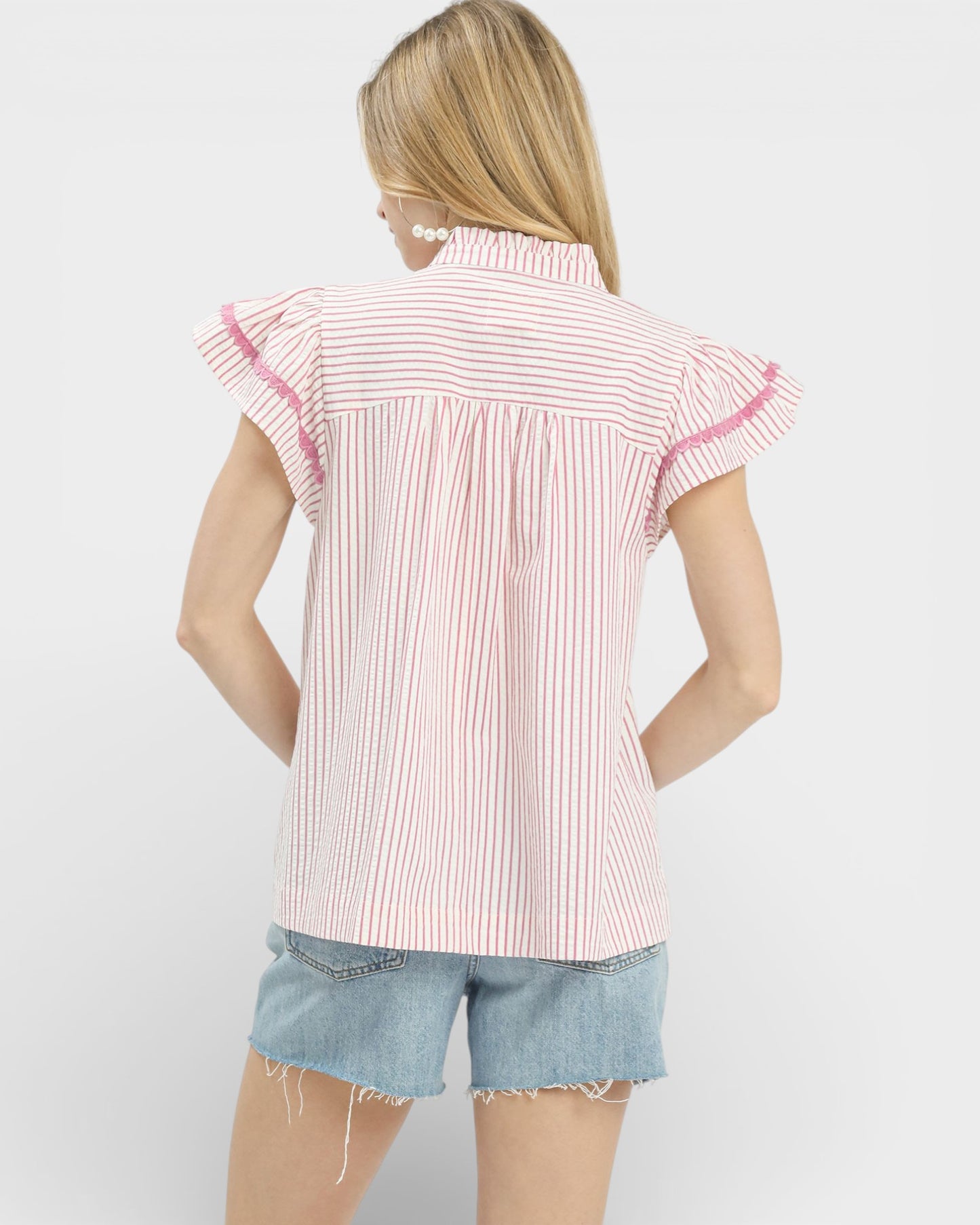 Woman wearing a pink and white striped shirt with ruffled sleeves on a white background