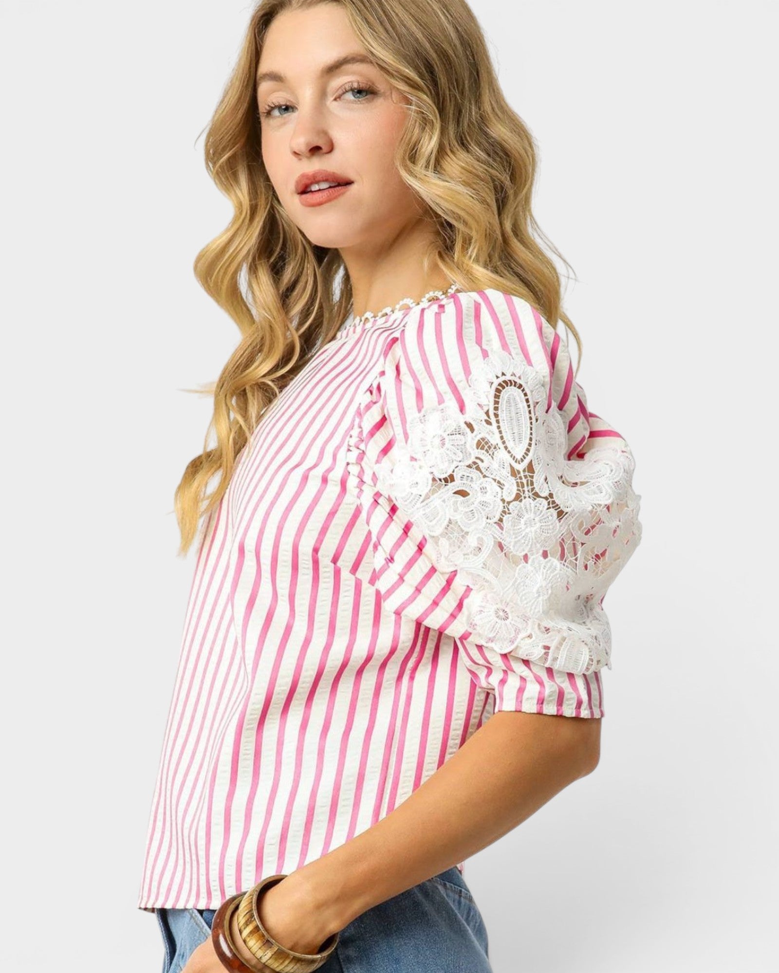 Woman wearing a pink and white striped blouse with lace details on a white background
