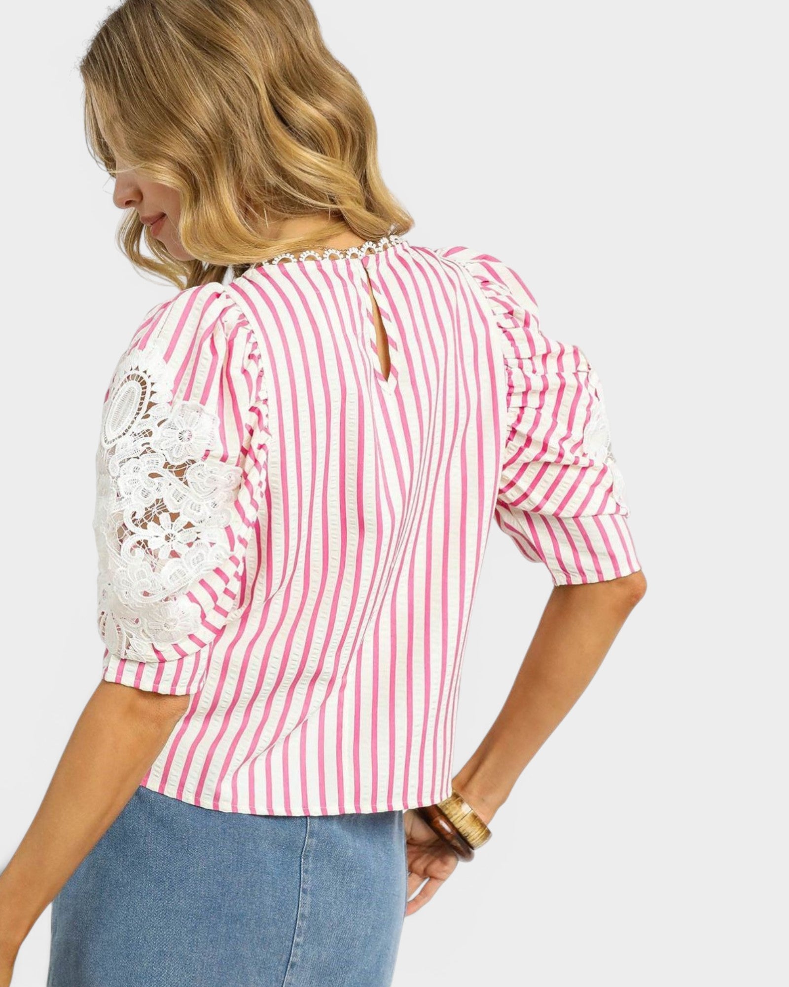 Woman wearing a pink and white striped blouse with lace details on a white background