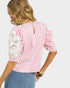 Woman wearing a pink and white striped blouse with lace details on a white background