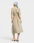 Woman wearing a beige dress with a belt and a patterned headscarf on a white background