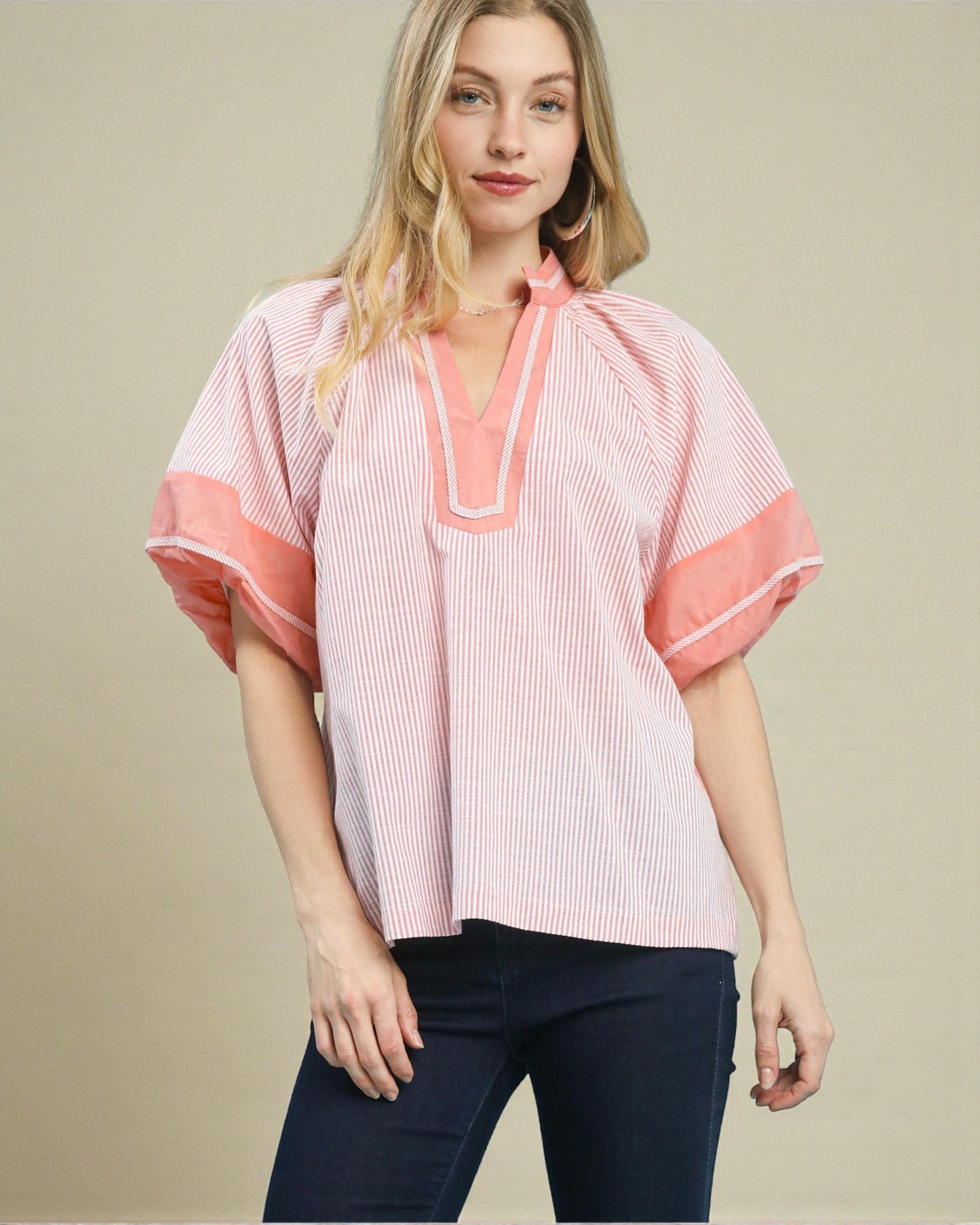 Woman wearing a pink and white striped blouse with a V-neckline on a beige background