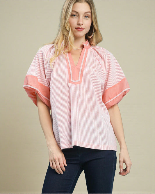 Woman wearing a pink and white striped blouse with a V-neckline on a beige background